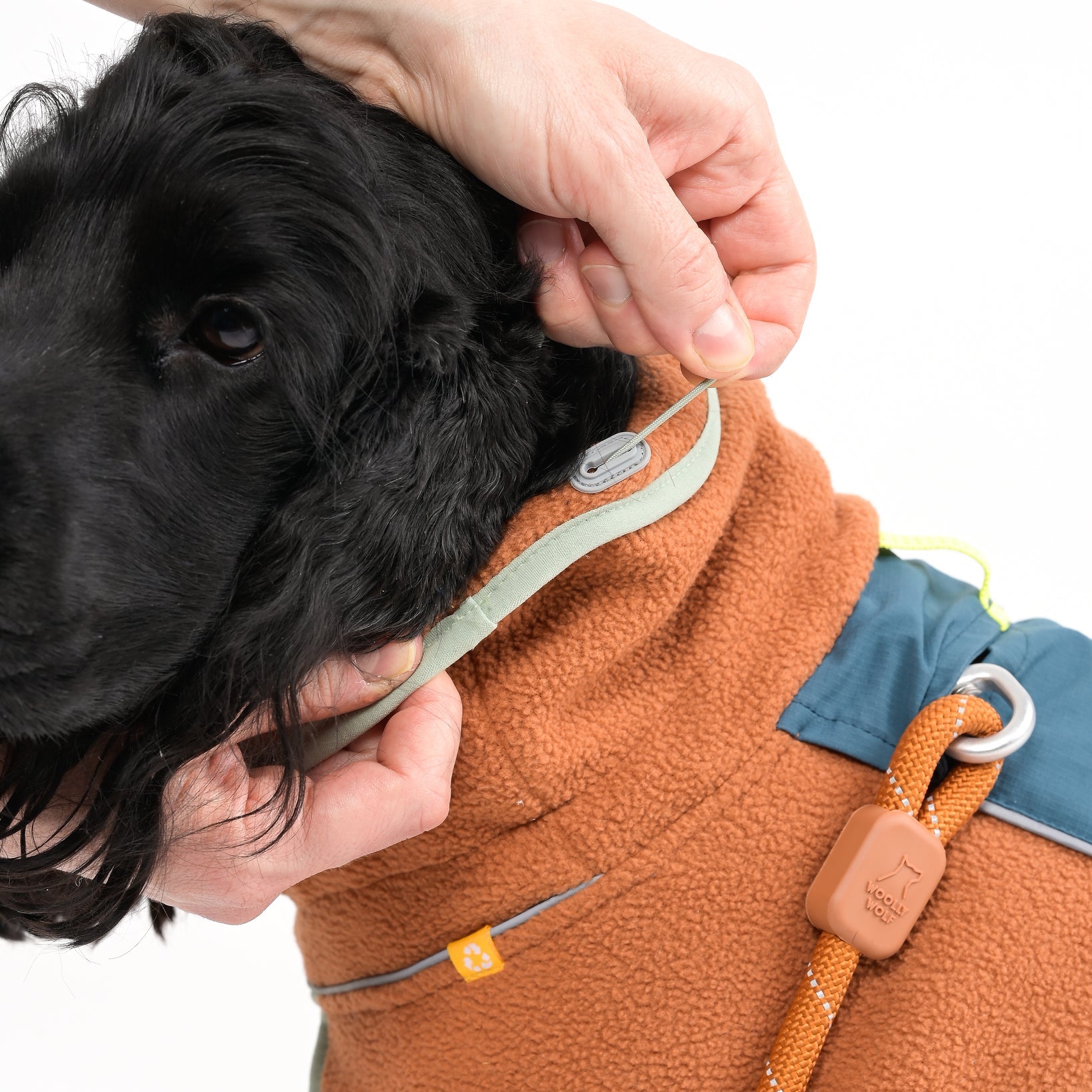 Dog wearing a brown fleece jacket , being adjusted by a person.