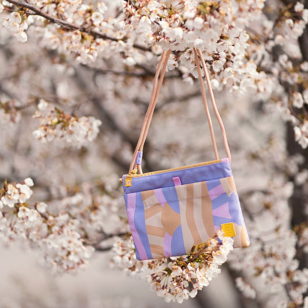 Pastel-colored purse with abstract patterns hanging on a branch of a blooming cherry blossom tree.