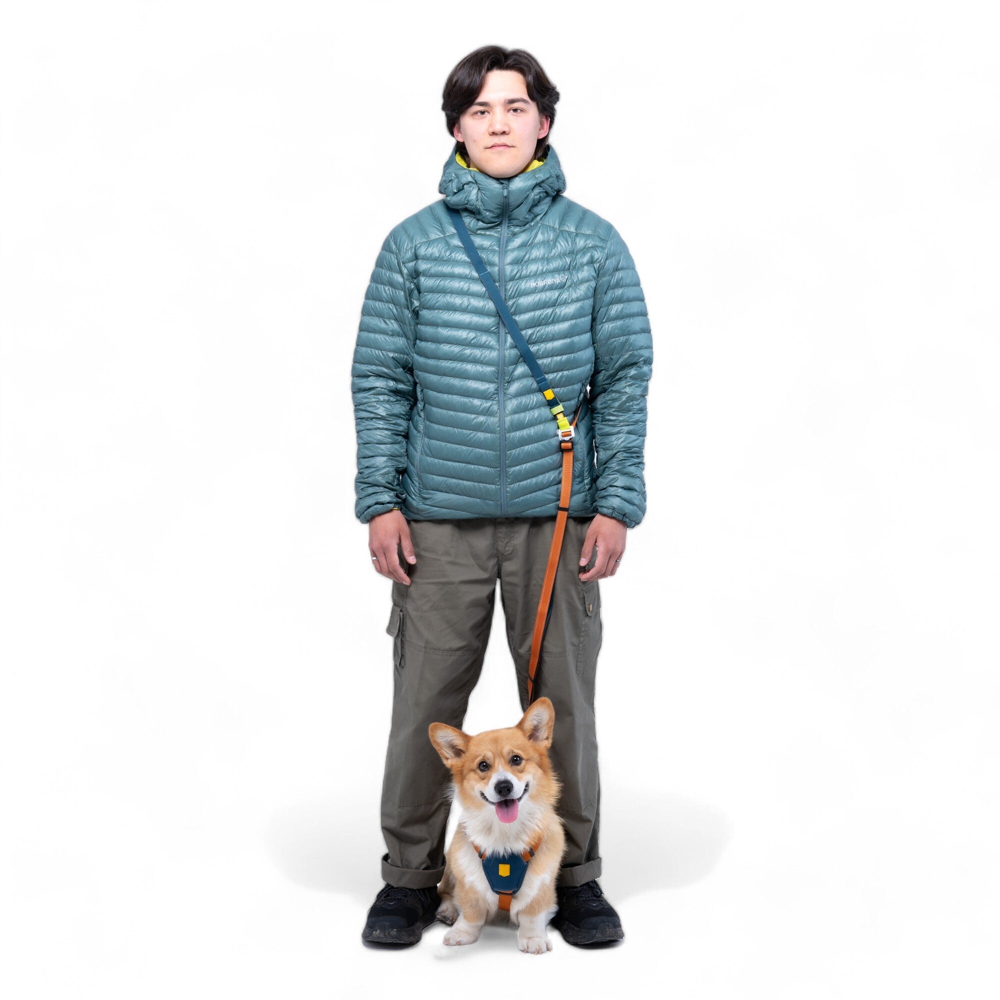 A person stands facing forward, holding the Color Block Multi-Use Dog Leash in Lime Mix, which is attached to a happy corgi sitting in front of them against a white background.